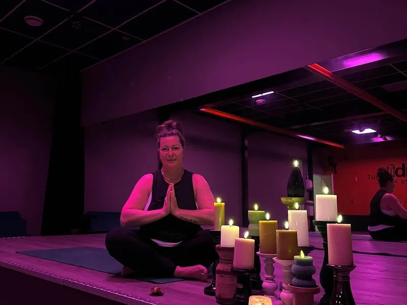 Yogalerares in meditatiehouding tussen brandende kaarsen in een sfeervol verlichte zaal